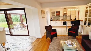 A modern living room with a glass coffee table, two armchairs, a sofa, and a kitchen in the background. - Seesternchen Fewo Nr. 1 (St. Peter-Ording)