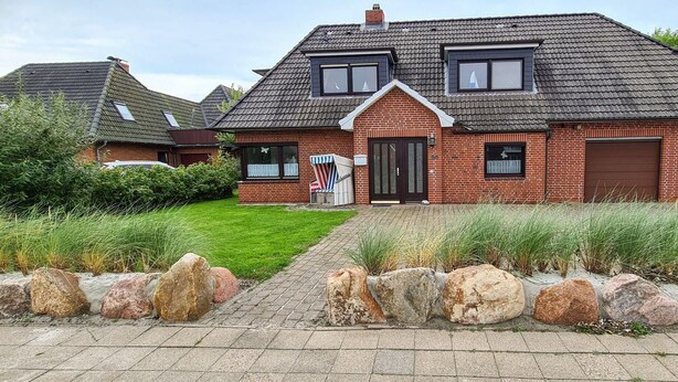 A two-story brick house with a sloped roof, a front garage, and a well-maintained lawn. - Seesternchen Fewo Nr. 1 (St. Peter-Ording)
