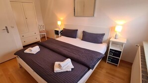 A neatly made bed with two pillows, a bedside table with a lamp, a wardrobe, and a radiator. - Seesternchen Fewo Nr. 1 (St. Peter-Ording)