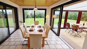 A dining area with a table set for four, surrounded by chairs, and a view of a garden through large glass doors. - Seesternchen Fewo Nr. 1 (St. Peter-Ording)
