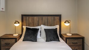A neatly made bed with two black pillows, a wooden headboard, and two bedside tables with lamps. - beachfront (Wasaga Beach)