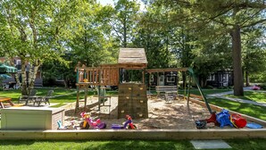 A playground with a wooden climbing structure, a swing set, and a sandbox area. - beachfront (Wasaga Beach)