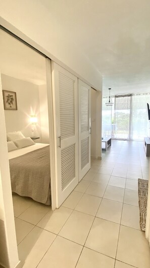 Habitación de hotel con cama, mesita de noche, lámpara de pared y puerta corrediza que da a un balcón.