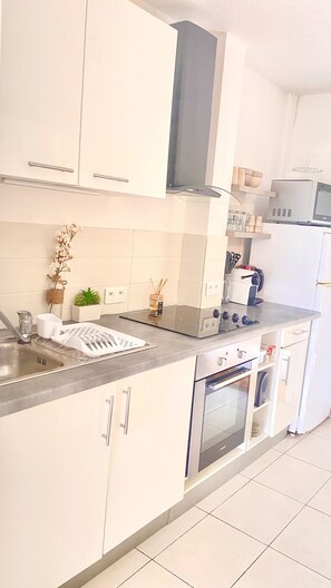 Una cocina moderna con armarios blancos, un lavamanos de acero inoxidable, un horno empotrado y un microondas.