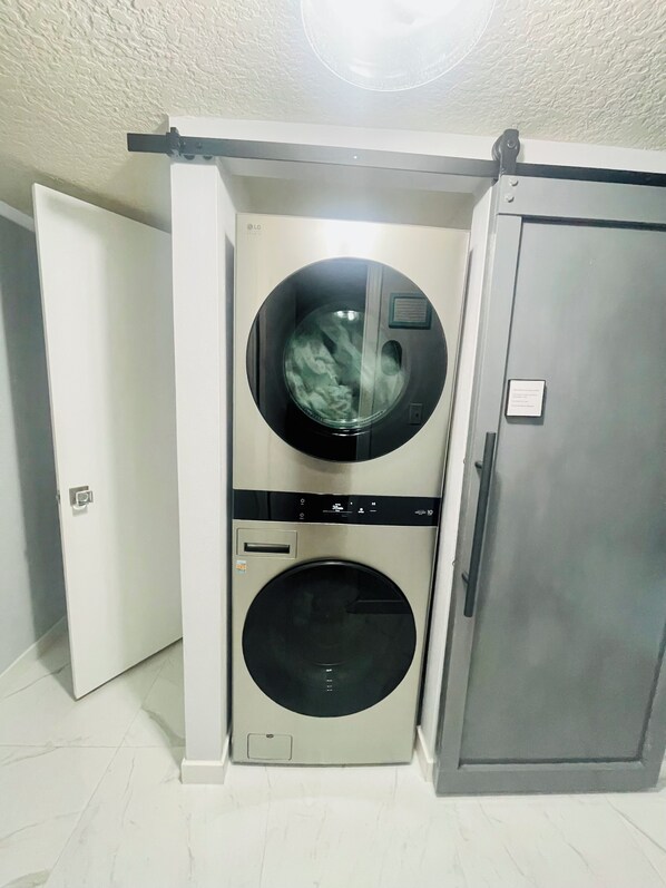 A compact, modern laundry room with a built-in washer and dryer, a metallic finish, and a door leading to another room. - Modern Resort-Style Stay (Orlando)