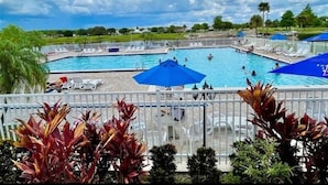 En swimmingpool med flere baner, omgivet af liggestole og parasoller, med udsigt til himlen og fjern vegetation.
