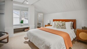 Ein Schlafzimmer mit einem großen Bett, einem Fenster mit Jalousien, einem Nachttisch mit Lampe und einem Sessel.
