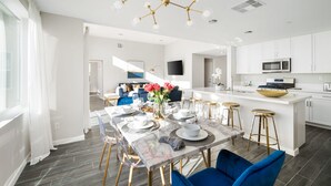 A modern kitchen with white cabinets, a central island with stools, and a dining area with a marble table and blue chairs.