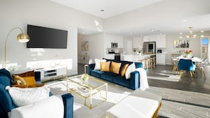 A modern living room with a blue sofa, a coffee table, and a flat-screen TV mounted on the wall.