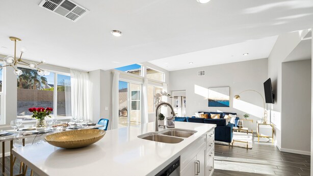 A modern kitchen with a large island, built-in dishwasher, and a dining area with a blue sofa and a TV.
