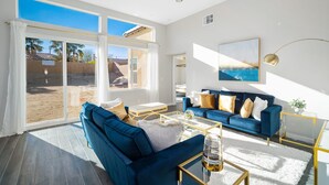 A spacious living room with a blue sofa, a coffee table, and a large window overlooking a sandy area.