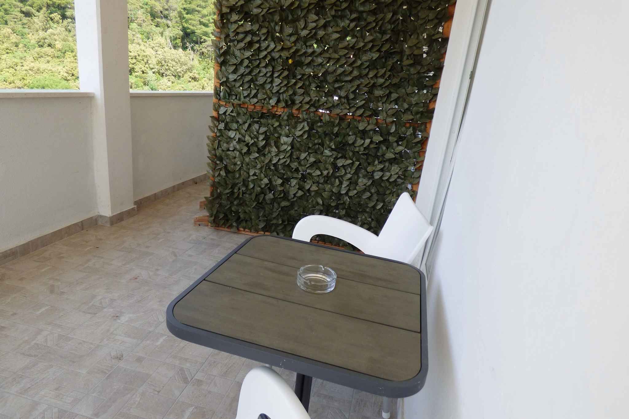 Een klein balkon met een tafel en stoelen, een decoratieve muur en uitzicht op groen.