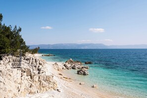 A rocky beach with clear water, a staircase leading down to the shore, and distant mountains.