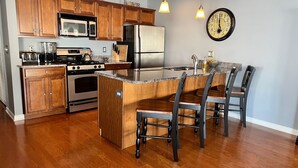 Una cucina con mobili in legno, elettrodomestici in acciaio inox, un'isola con piano di lavoro in granito e un orologio a parete.