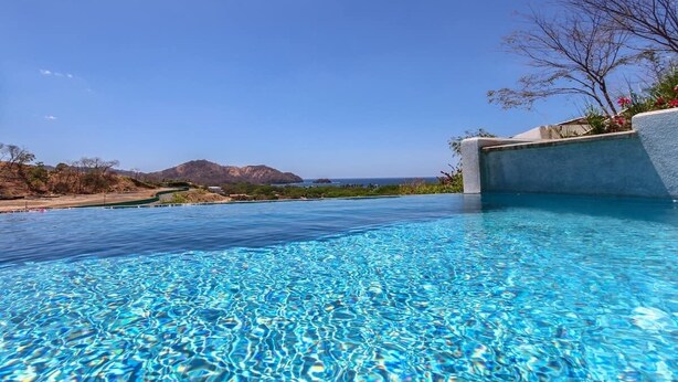 A clear blue pool with a view of the ocean and mountains in the background.
