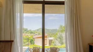 A bedroom with a large window, a bed, and two wicker chairs facing a pool.