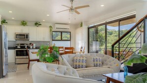 A modern kitchen with white cabinets, a microwave, and a dining area with a white sofa and chairs.