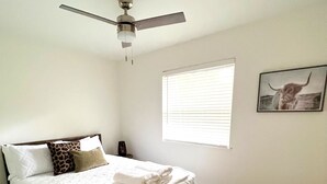 A bedroom with a bed, a ceiling fan, a window with blinds, and a framed picture on the wall. - *Aviate to the Lake* Downtown Lake Geneva (LAKE GENEVA)