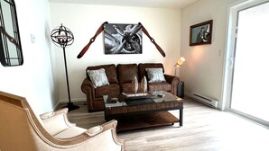 A living room with a brown leather sofa, a glass coffee table, and a wooden chair. - *Aviate to the Lake* Downtown Lake Geneva (LAKE GENEVA)