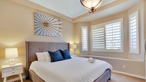 A bedroom with a large bed, two bedside tables, a wall-mounted artwork, and a ceiling light fixture.