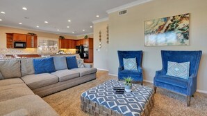 A spacious living room with a large sectional sofa, two blue armchairs, and a patterned ottoman.