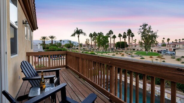 A balcony with a view of a landscaped area, palm trees, and a distant mountain range.
