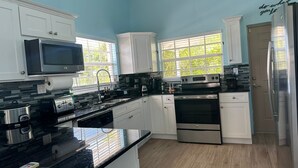 A modern kitchen with white cabinets, a black countertop, stainless steel appliances, and a window with a view of greenery. - Beautiful villa West with pool- 5 minutes to Gracebay beach (Providenciales)