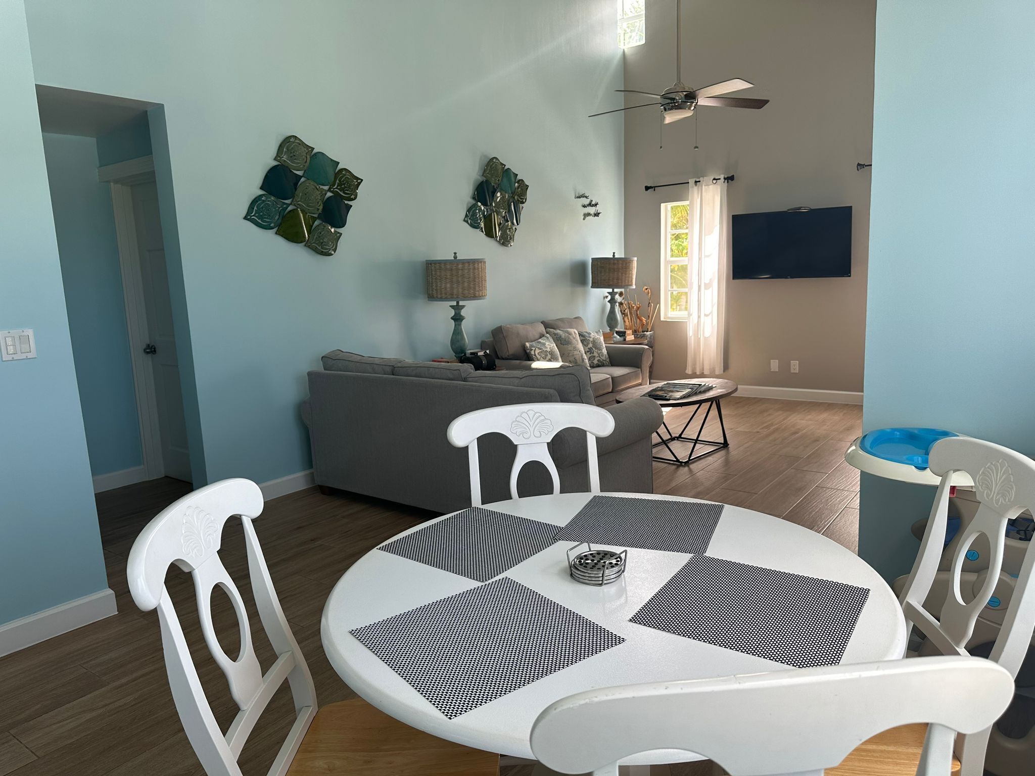 A modern living room with a round dining table, white chairs, a grey sofa, and a ceiling fan.