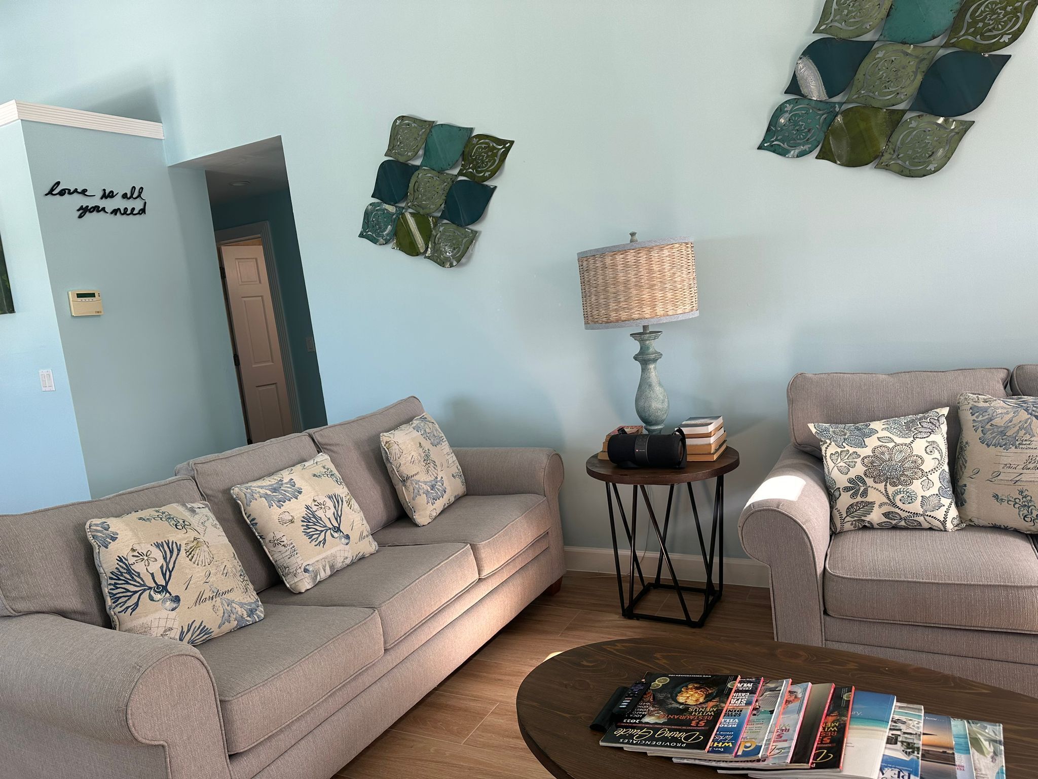 Un salon avec deux canapés, une table basse avec des magazines, une lampe et des œuvres d’art décoratives accrochées au mur.