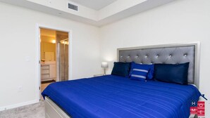 A bedroom with a large bed, a nightstand, a lamp, and a door leading to a bathroom. - Stunning Condo with Great View - Close to Disney! (Kissimmee)