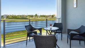 A balcony with wicker furniture, a small table, and two framed pictures on the wall. - Stunning Condo with Great View - Close to Disney! (Kissimmee)