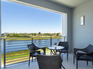A balcony with wicker furniture, a small table, and two framed pictures on the wall. - Stunning Condo with Great View - Close to Disney! (Kissimmee)