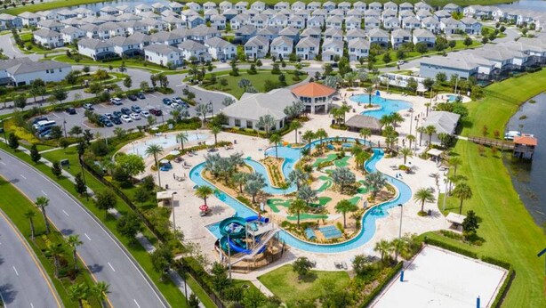 An aerial view of a residential area with a large swimming pool complex, surrounded by single-family homes and a body of water. - Stunning Condo with Great View - Close to Disney! (Kissimmee)