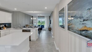 A modern kitchen with white cabinetry, a large island, and a dining area with blue chairs.