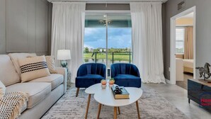 A modern living room with a sofa, two armchairs, a coffee table, and a view of a golf course through large windows.
