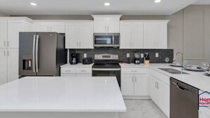 A modern kitchen with white cabinets, stainless steel appliances, a central island, and a dishwasher.