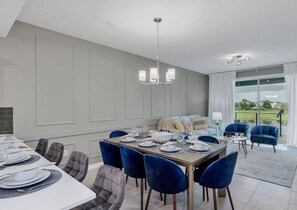 Un comedor con una gran mesa dispuesta para seis comensales, sillas azules y un sofá al fondo.