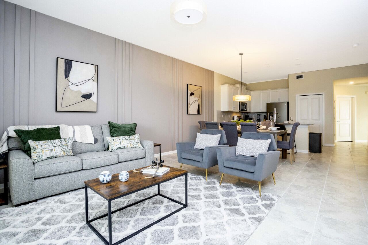 A modern living room with a grey sofa, two armchairs, a coffee table, and a kitchen in the background.