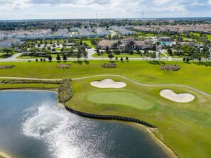 Un campo de golf con búnkeres, un estanque y una zona residencial al fondo.