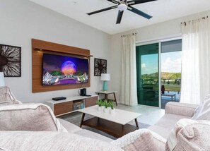 A modern living room with a flat-screen TV, a ceiling fan, a sliding glass door to a balcony, and a minimalist decor.