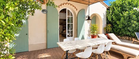 An outdoor patio with a table and chairs, a hanging light fixture, and a covered area with a thatched roof.