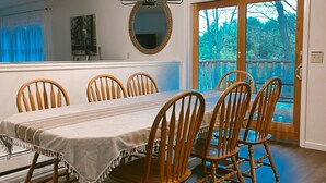 A dining area with a long table, wooden chairs, a chandelier, a mirror, and a view of the outdoors through a glass door.