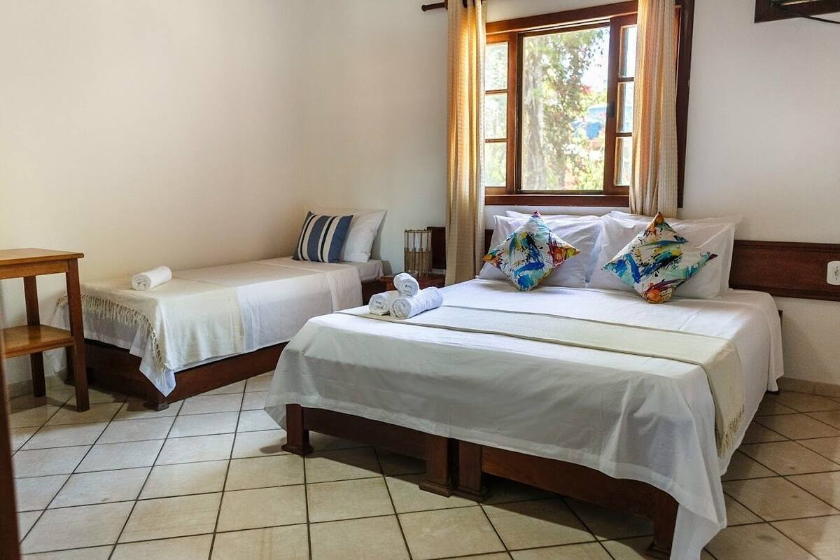 Una camera d'albergo con due letti singoli, un comodino in legno e una finestra con tende.