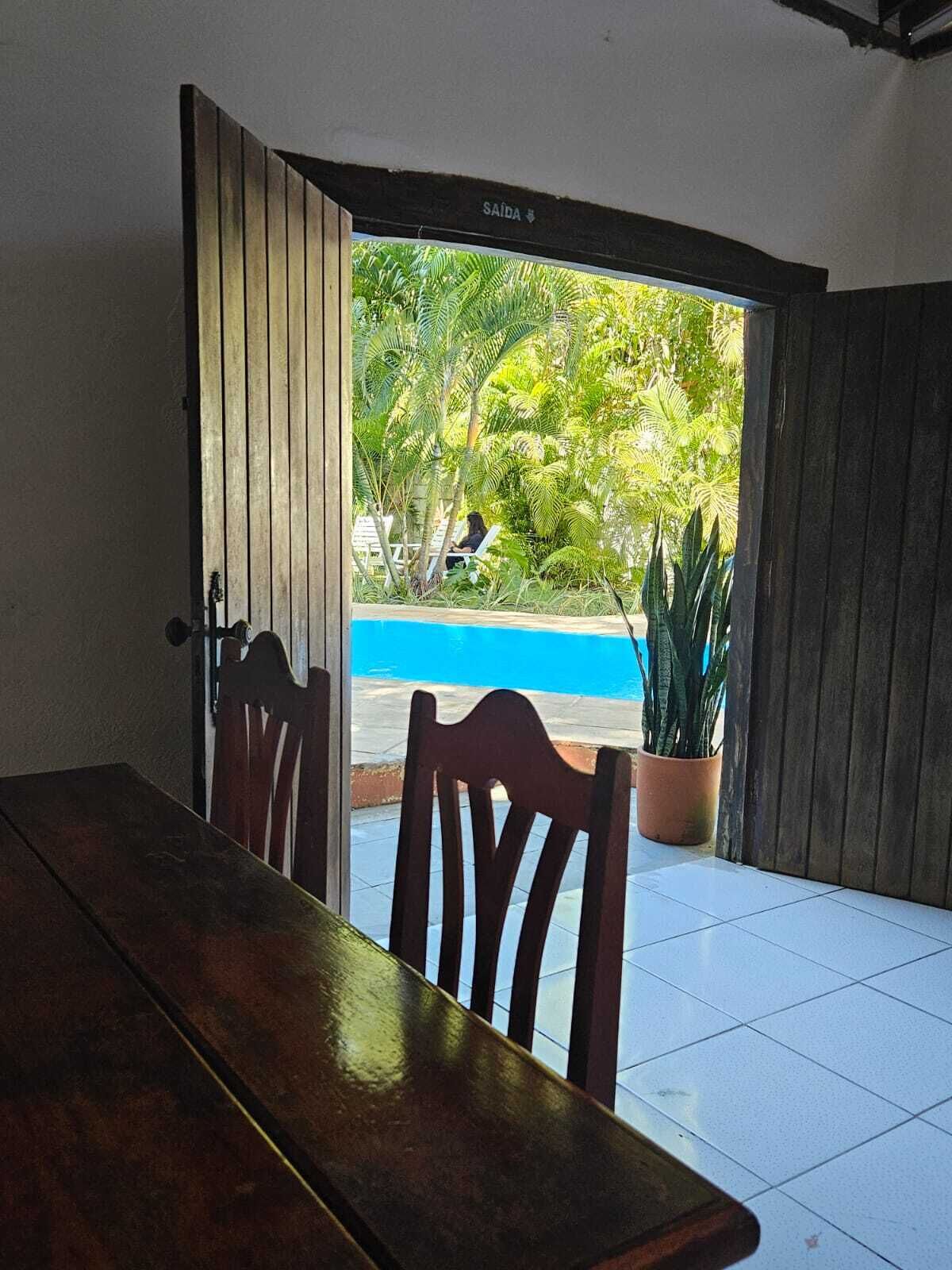 A room with a wooden table and chairs, a view of a swimming pool, and a potted plant.