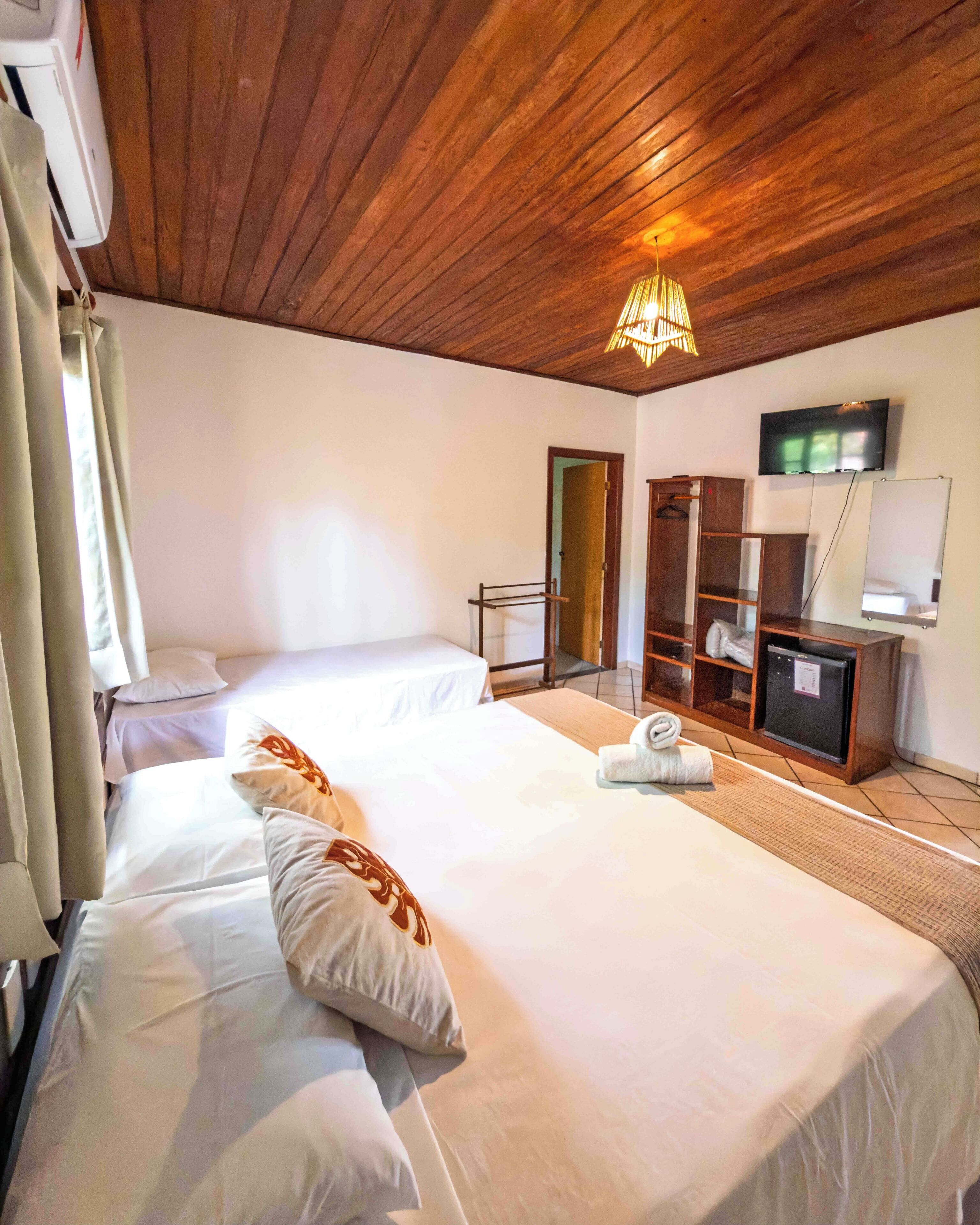 A hotel room with two beds, a wooden ceiling, a TV, and a wardrobe.