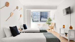 Una habitación de hotel moderna con dos camas, un televisor, una ventana con vista a la ciudad y una pequeña mesa con una planta.