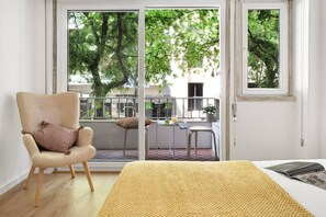 A room with a bed, a chair, a small table with a plant, and a view of trees through a sliding door. - Bright Apartment in Central Lisbon | 3 bedrooms by Lisbeyond (Lisboa)