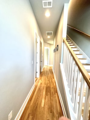 Staircase leads to doors along a well-lit hallway with a wooden floor.