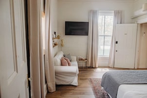 A bedroom with a bed, a sofa, a TV mounted on the wall, and a door.