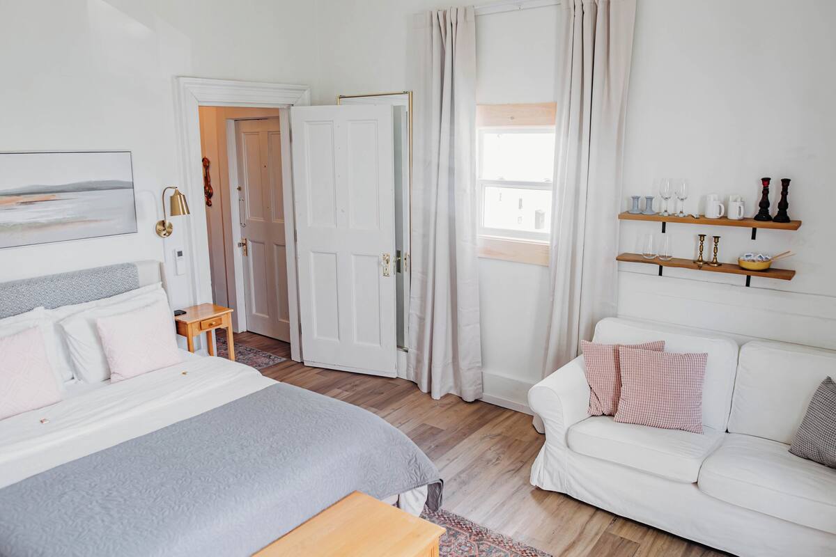 A bedroom with a bed, bedside table, and a white sofa.